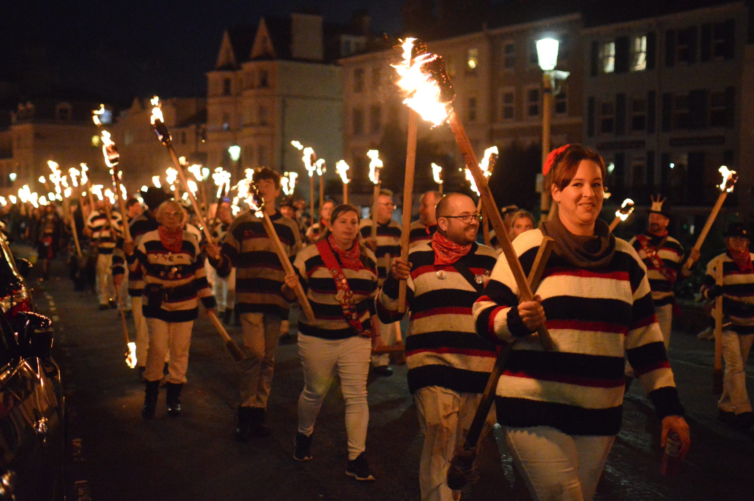 EBS members wearing striped smuggler jumpers, walking in ranks of three carrying burning torches